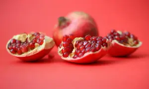 Czy pies może jeść granat? Na czerwonym tle leżą połówki granatu, pełne soczystych nasion.