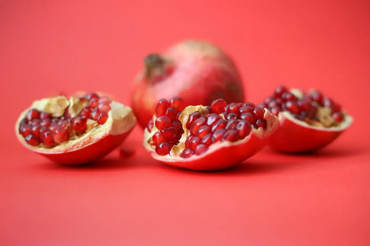 Czy pies może jeść granat? Na czerwonym tle leżą połówki granatu, pełne soczystych nasion.