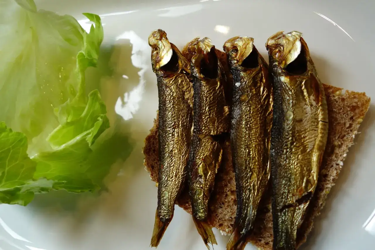 Na talerzu liść sałaty i kromka chleba z kilkoma szprotkami. Czy szprotki są zdrowe? Tak, to bogactwo kwasów omega-3.
