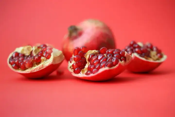 Czy pies może jeść granat? Na czerwonym tle leżą połówki granatu, pełne soczystych nasion.
